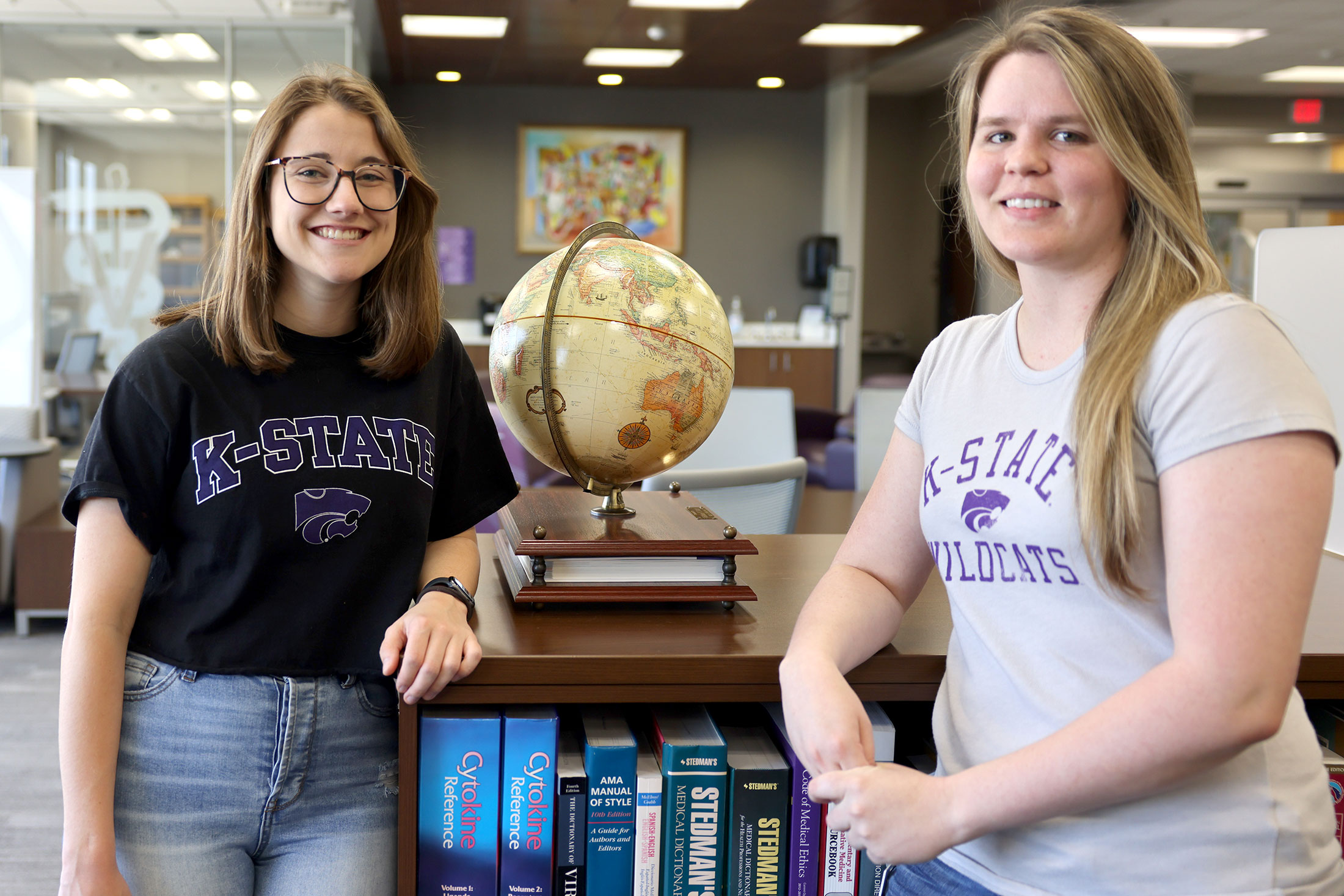 Students stand by bookshlef with globe on top