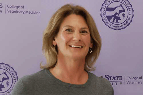 A cheerful woman poses with a smile against a purple wall backdrop.