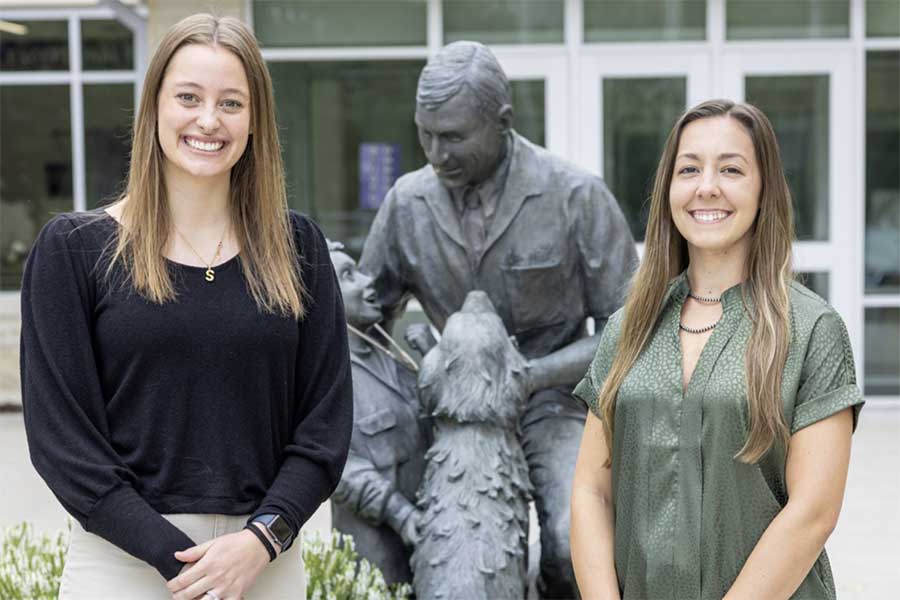 Two students stand next to statue in front of veterinary college