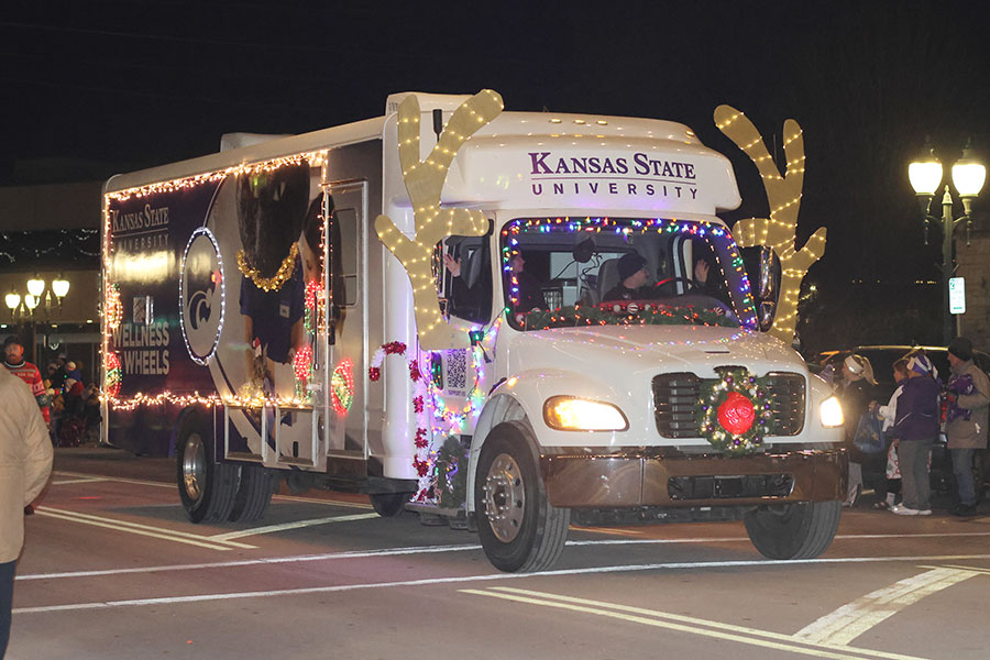 Wellness On Wheels, or WOW, vehicle decorated with lights drives down street during holiday parade
