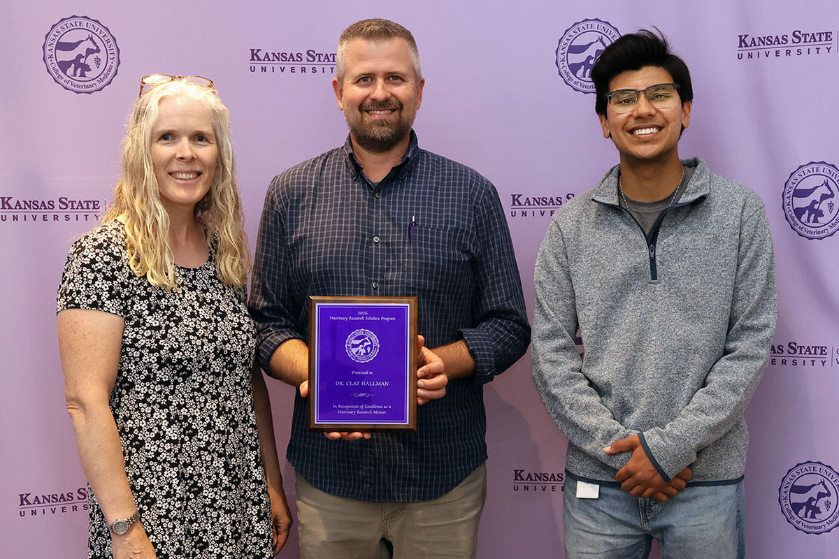 Two faculty members and a student pose in front of a step-repeat banner