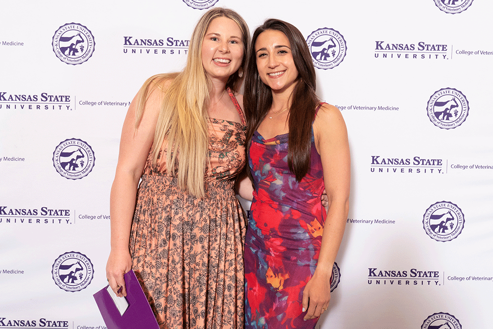 Two people stand in front of a backdrop smiling.