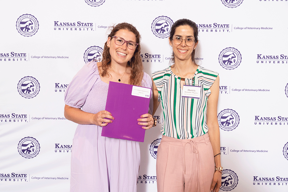 Two people stand in front of a backdrop smiling.