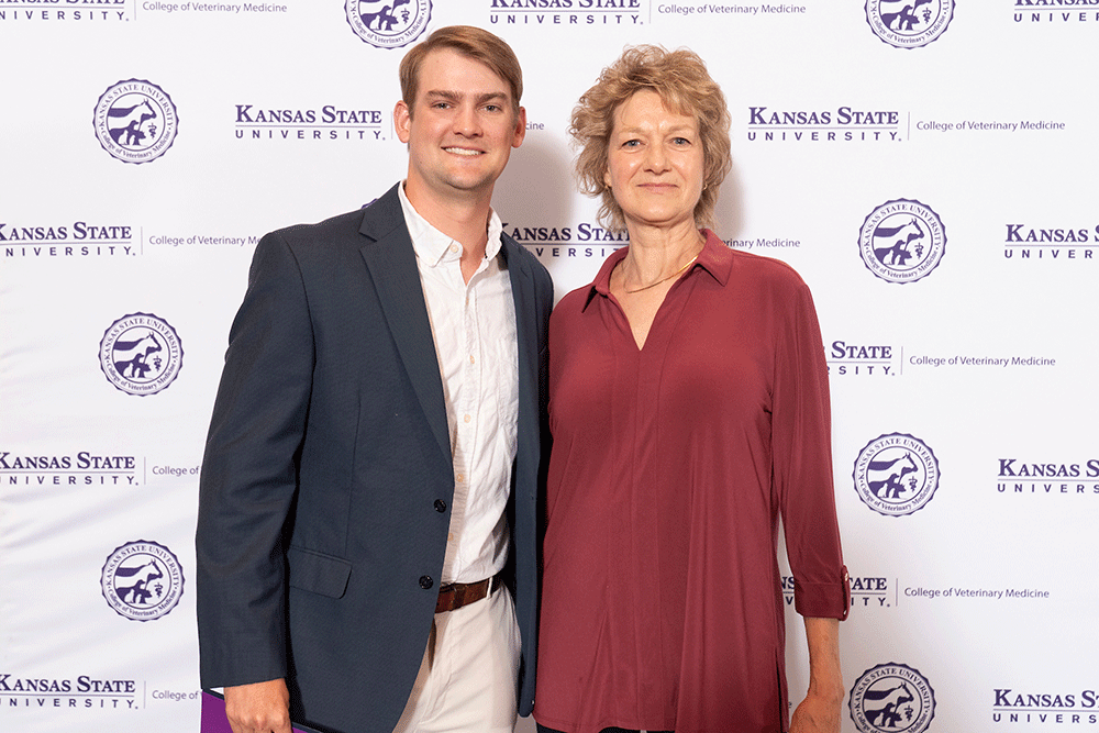 Two people stand in front of a backdrop smiling.