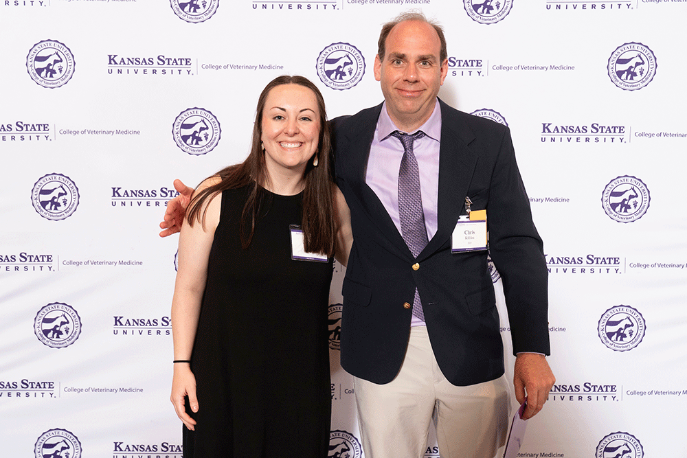 Two people stand in front of a backdrop smiling.