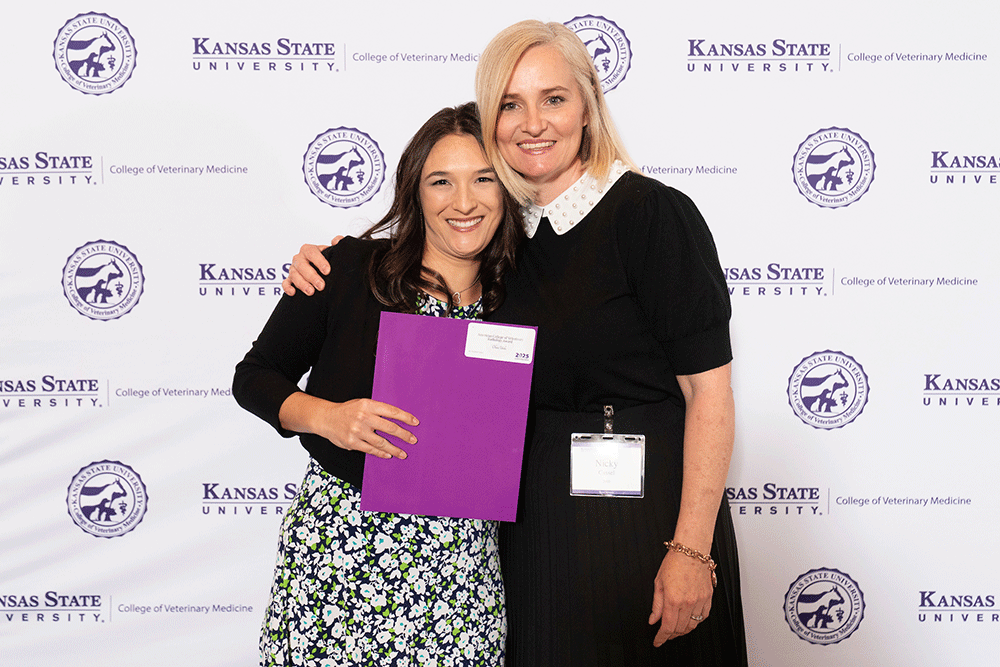 Two people stand in front of a backdrop smiling.