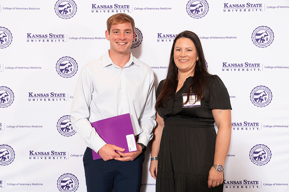 Two people stand in front of a backdrop smiling.