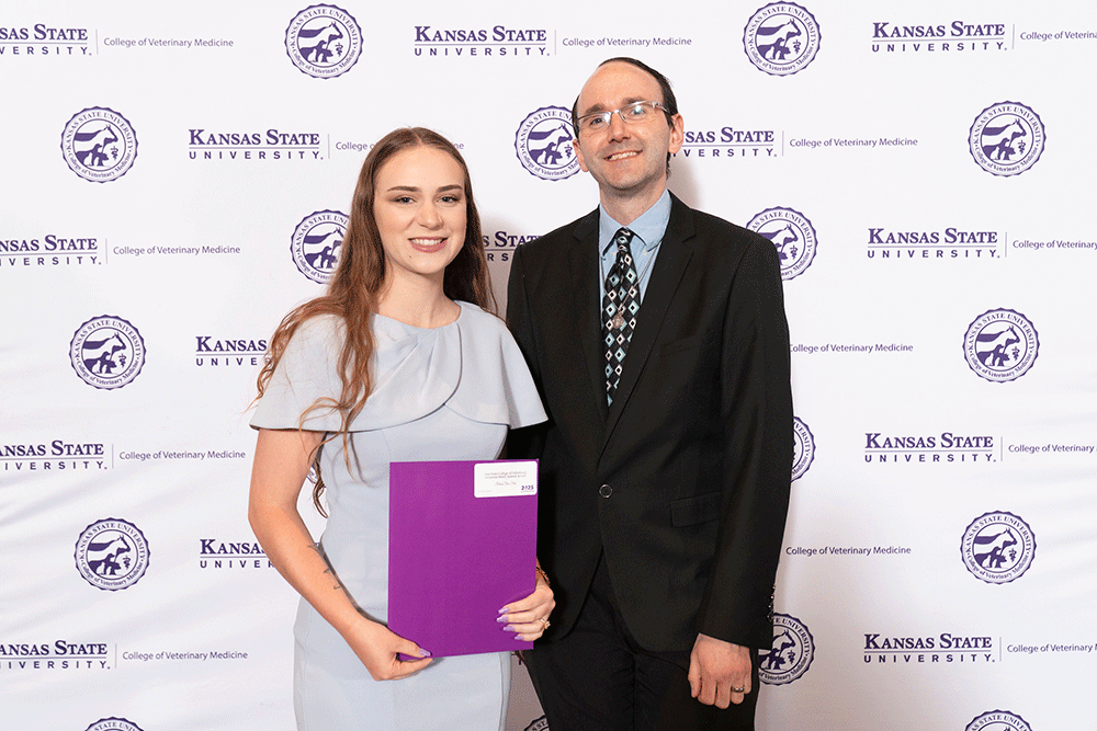 Two people stand in front of a backdrop smiling.