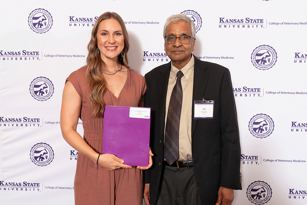 Two people stand in front of a backdrop smiling.