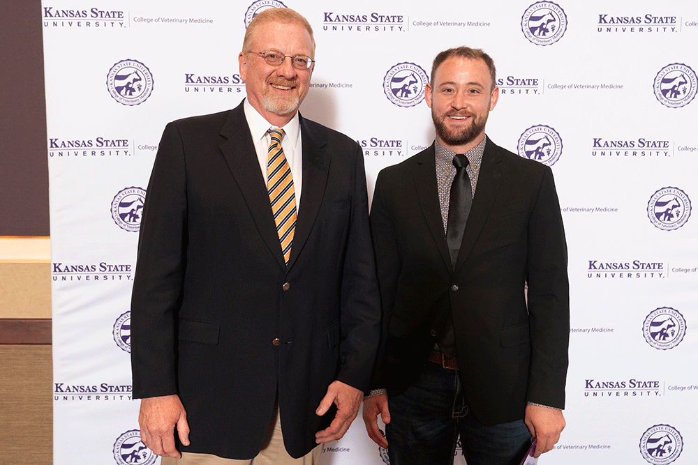 Two people stand in front of a backdrop smiling.