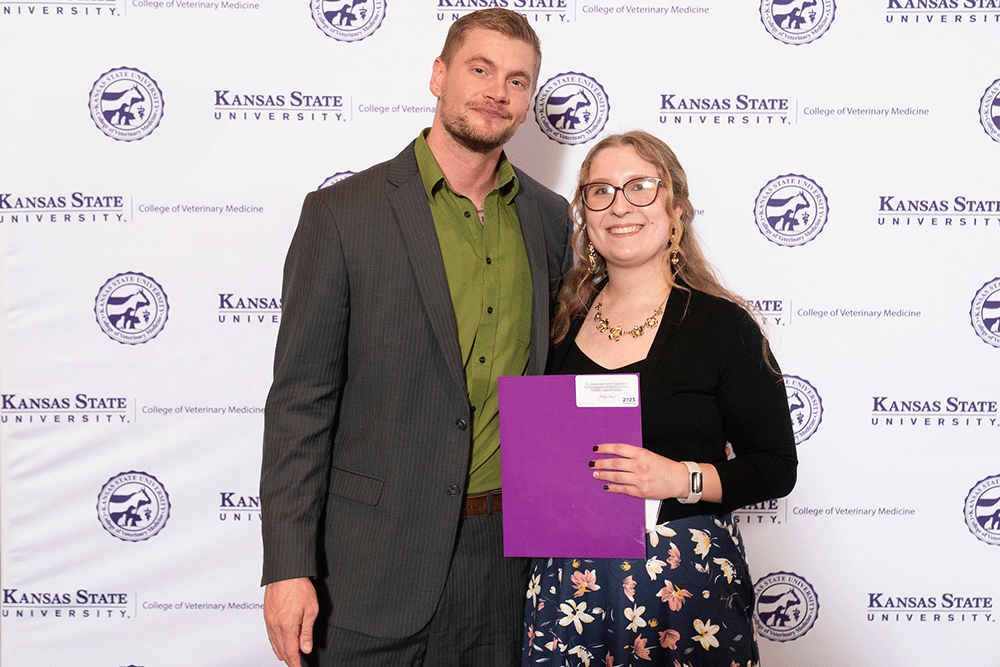 Two people stand in front of a backdrop smiling.