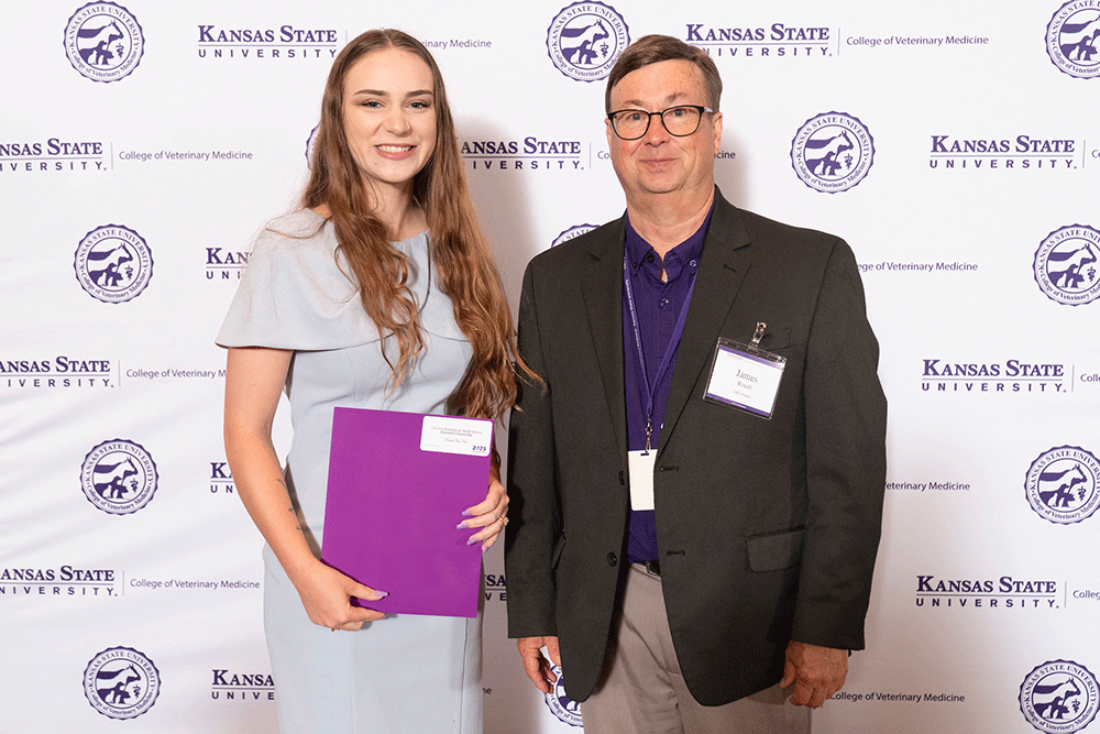 Two people stand in front of a backdrop smiling.