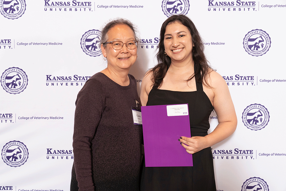 Two people stand in front of a backdrop smiling.