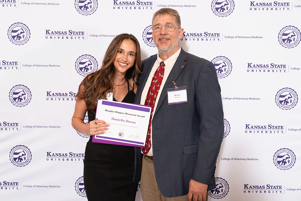 Two people stand in front of a backdrop smiling.