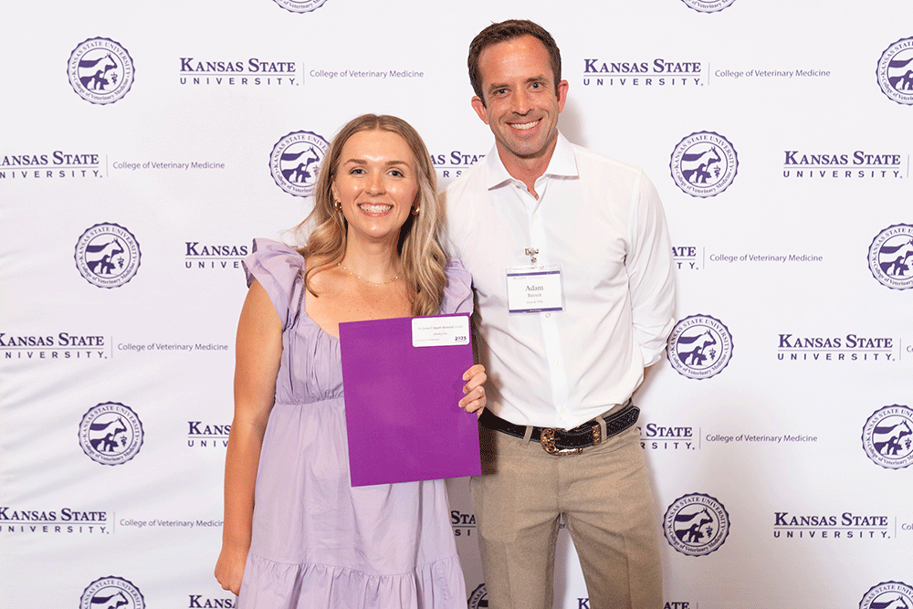 Two people stand in front of a backdrop smiling.