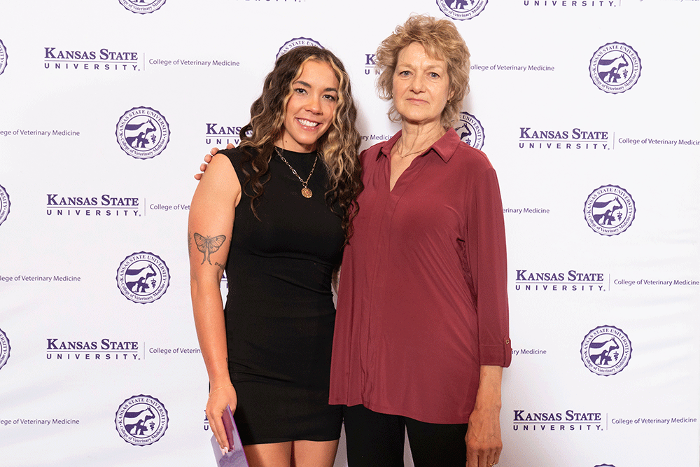 Two people stand in front of a backdrop smiling.