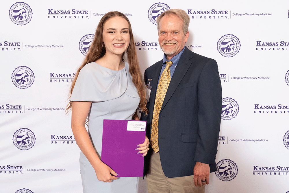 Two people stand in front of a backdrop smiling.