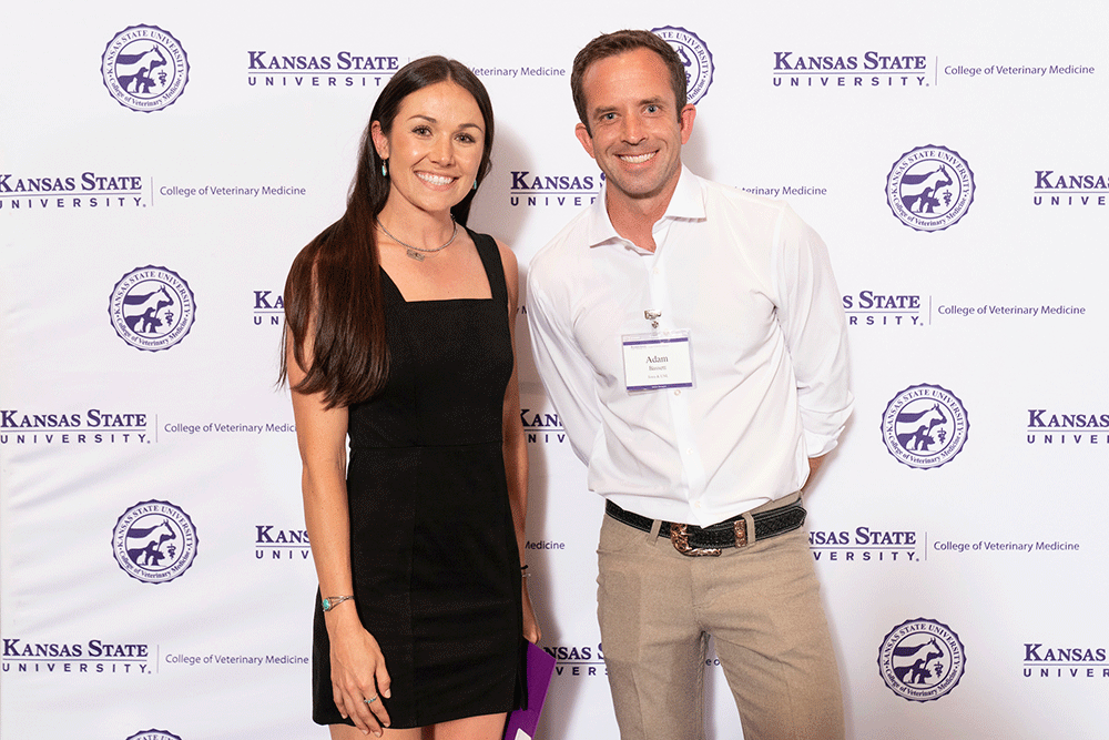 Two people stand in front of a backdrop smiling.