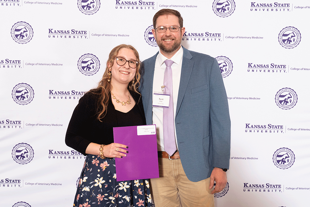 Two people stand in front of a backdrop smiling.