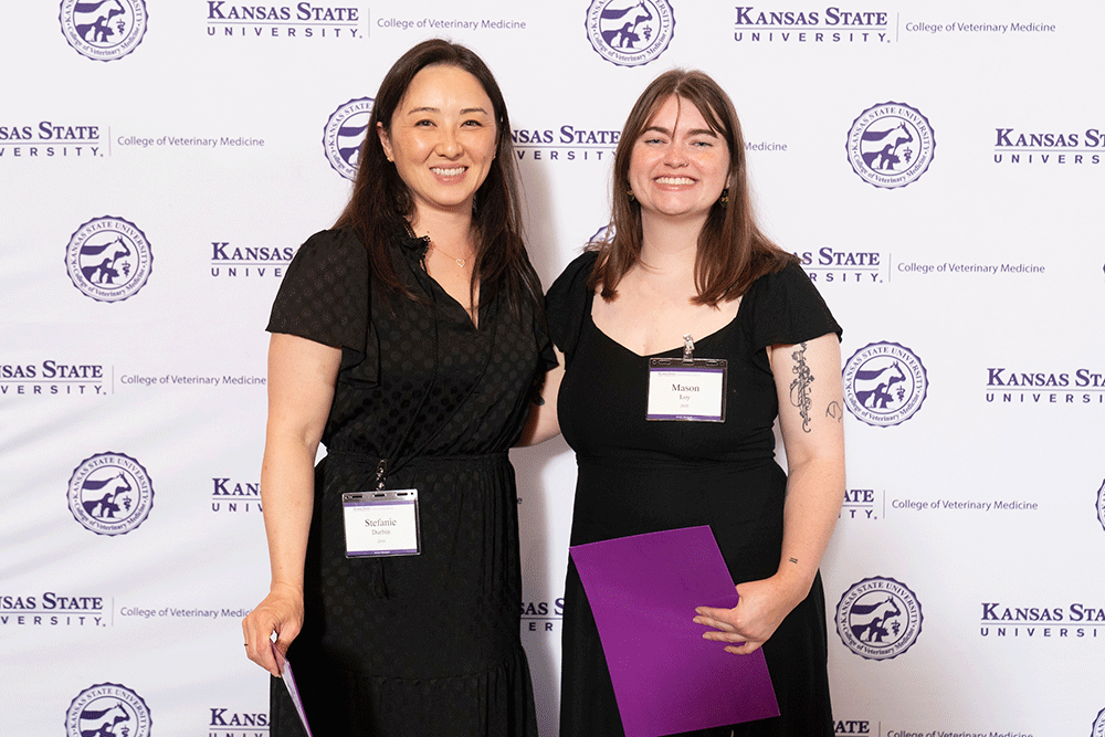Two people stand in front of a backdrop smiling.