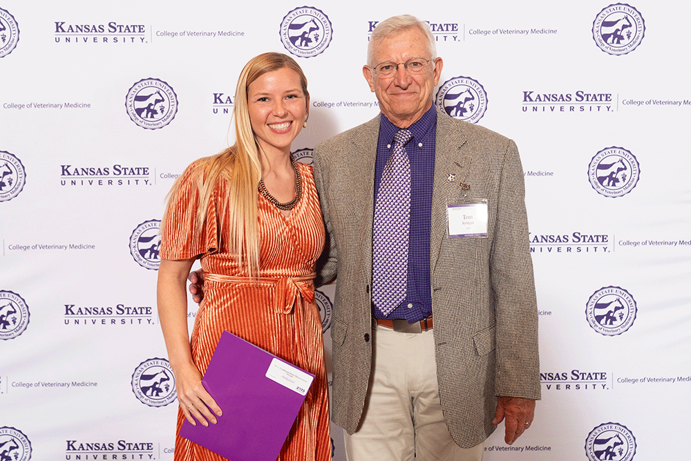 Two people stand in front of a backdrop smiling.