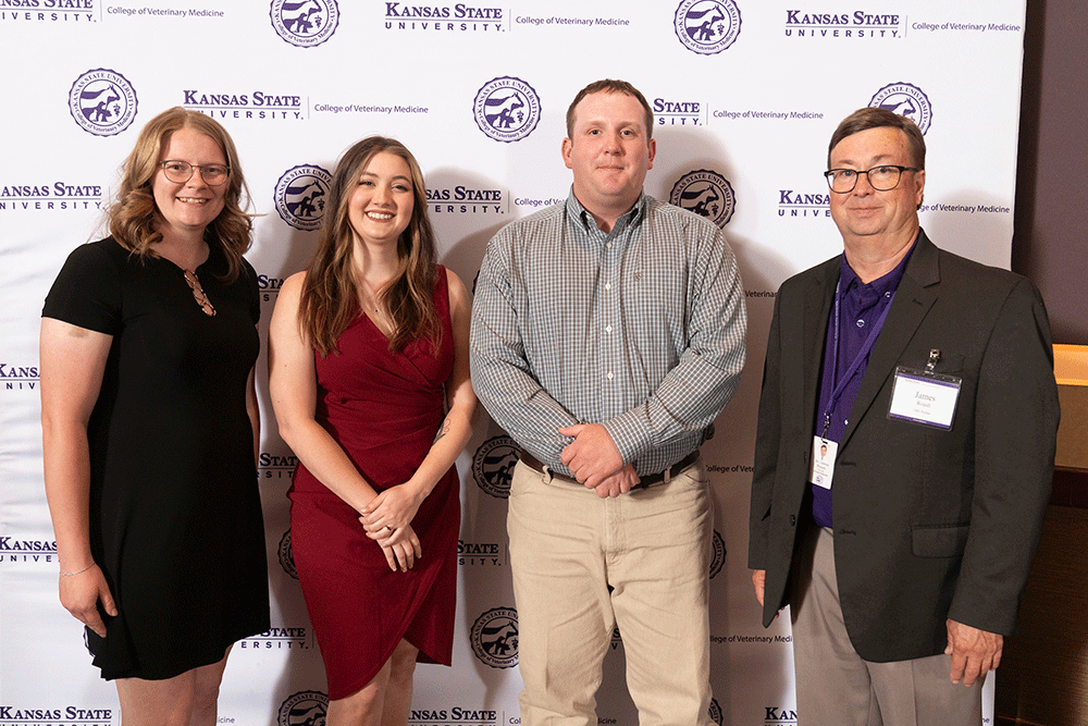 Four people stand in front of a backdrop smiling.