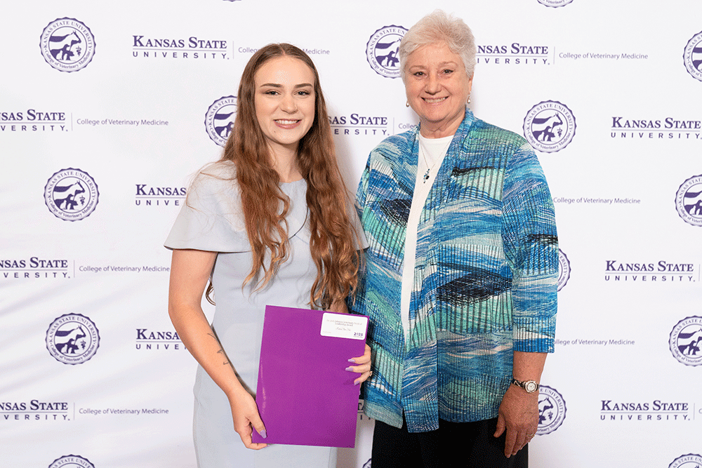 Two people stand in front of a backdrop smiling.