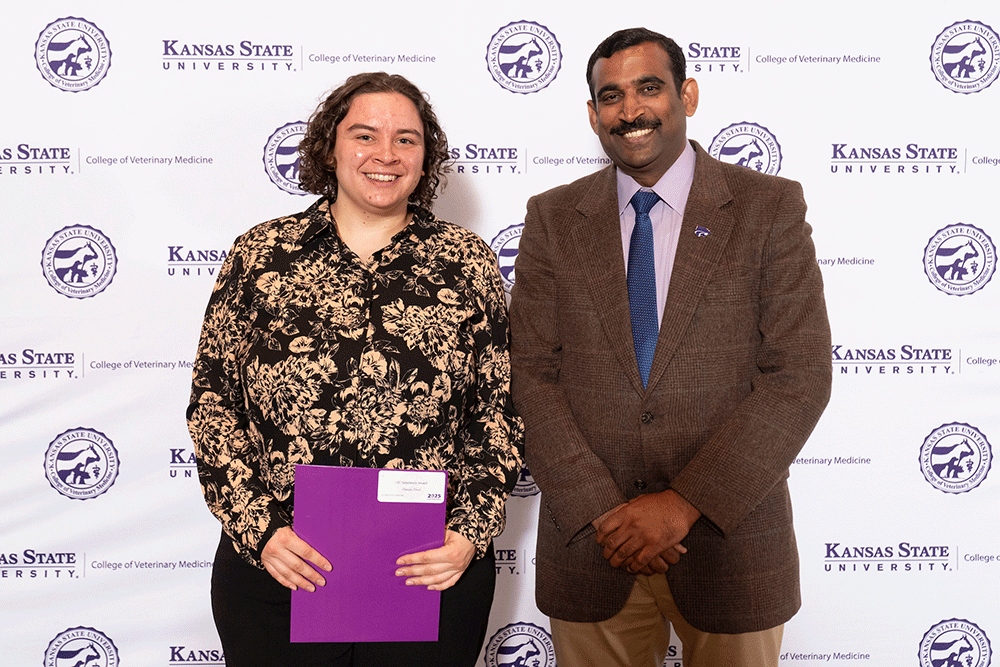 Two people stand in front of a backdrop smiling.