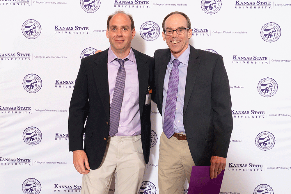 Two people stand in front of a backdrop smiling.