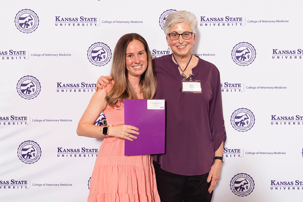 Two people stand in front of a backdrop smiling.