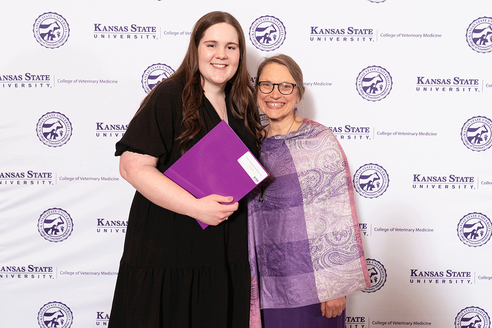 Two people stand in front of a backdrop smiling.