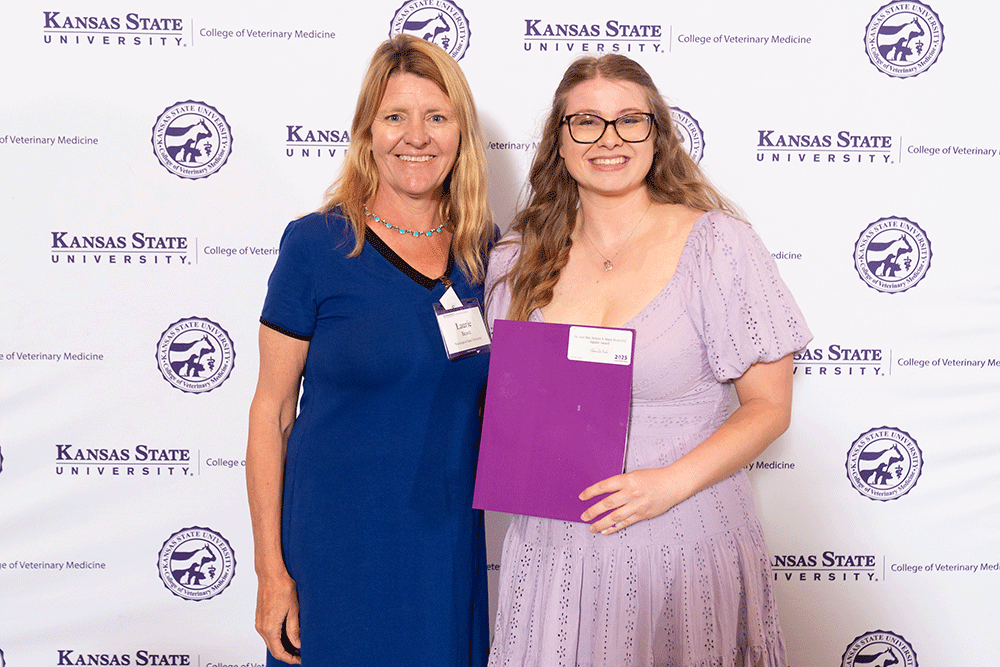 Two people stand in front of a backdrop smiling.