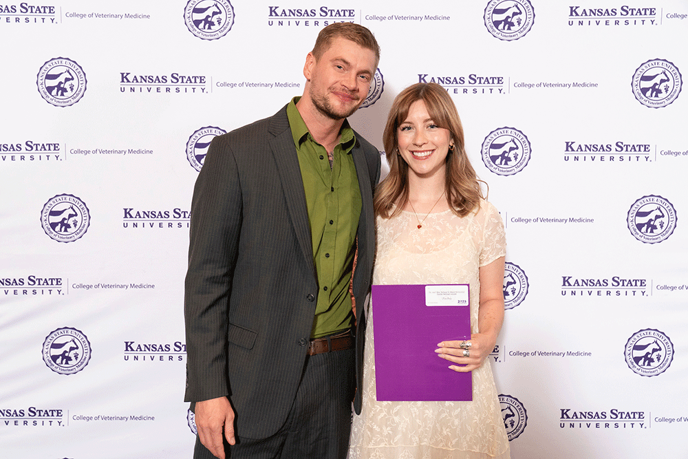 Two people stand in front of a backdrop smiling.