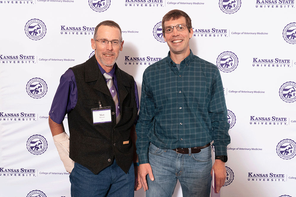 Two people stand in front of a backdrop smiling.