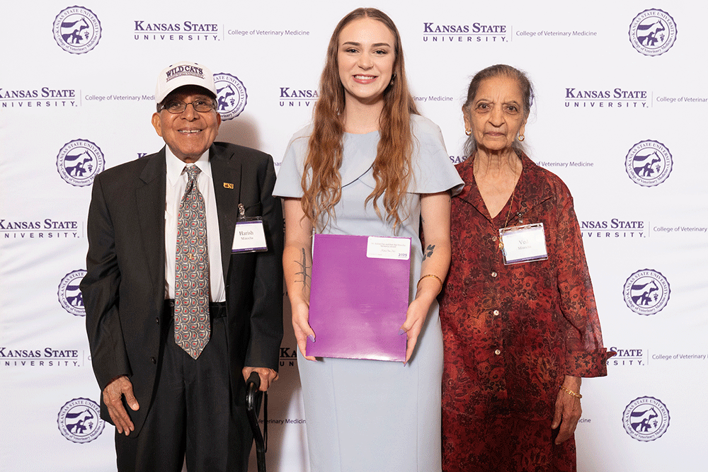 Three people stand in front of a backdrop smiling.