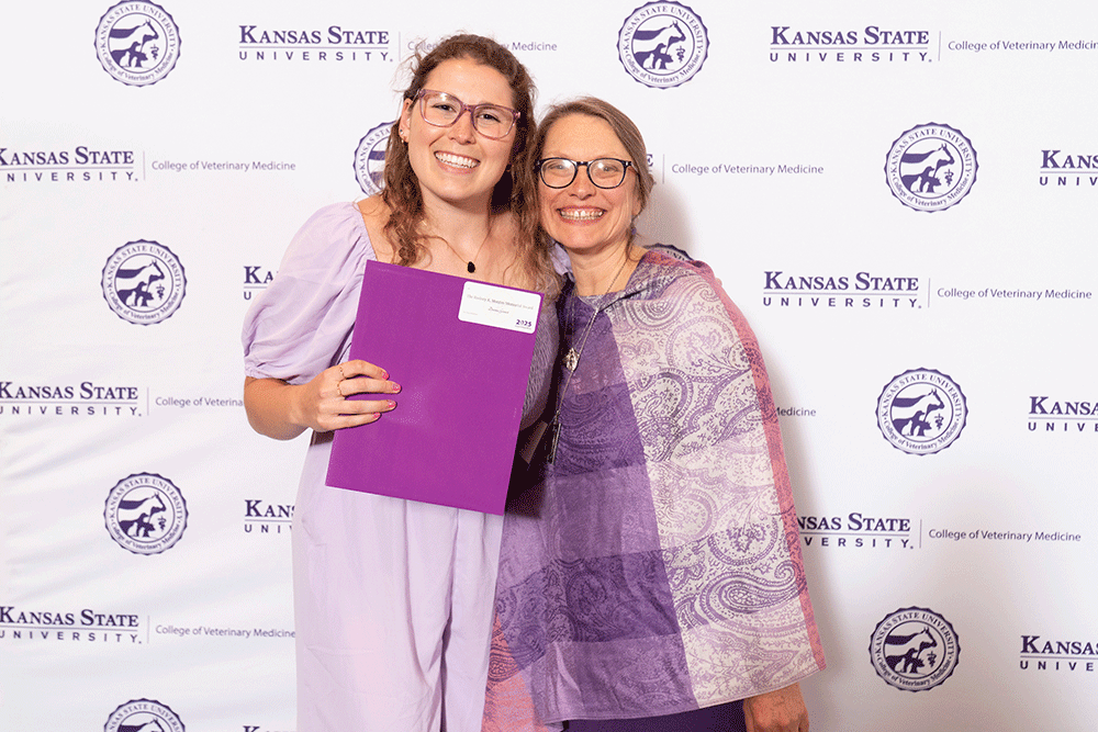 Two people stand in front of a backdrop smiling.