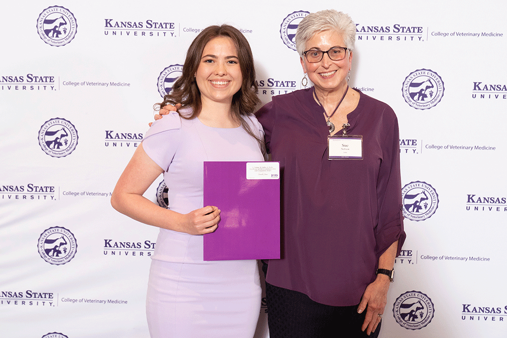 Two people stand in front of a backdrop smiling.