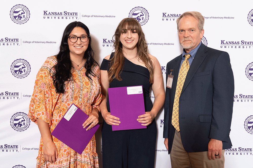 Three people stand in front of a backdrop smiling.
