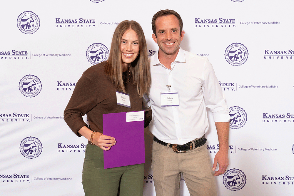 Two people stand in front of a backdrop smiling.
