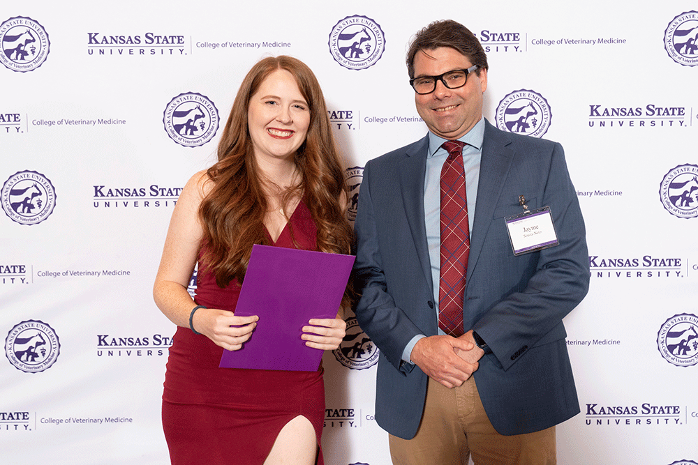 Two people stand in front of a backdrop smiling.