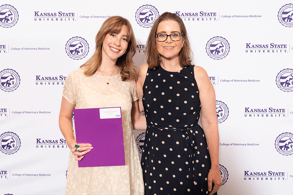 Two people stand in front of a backdrop smiling.