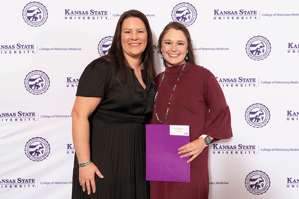 Two people stand in front of a backdrop smiling.
