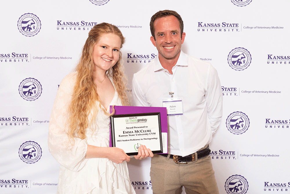Two people stand in front of a backdrop smiling.