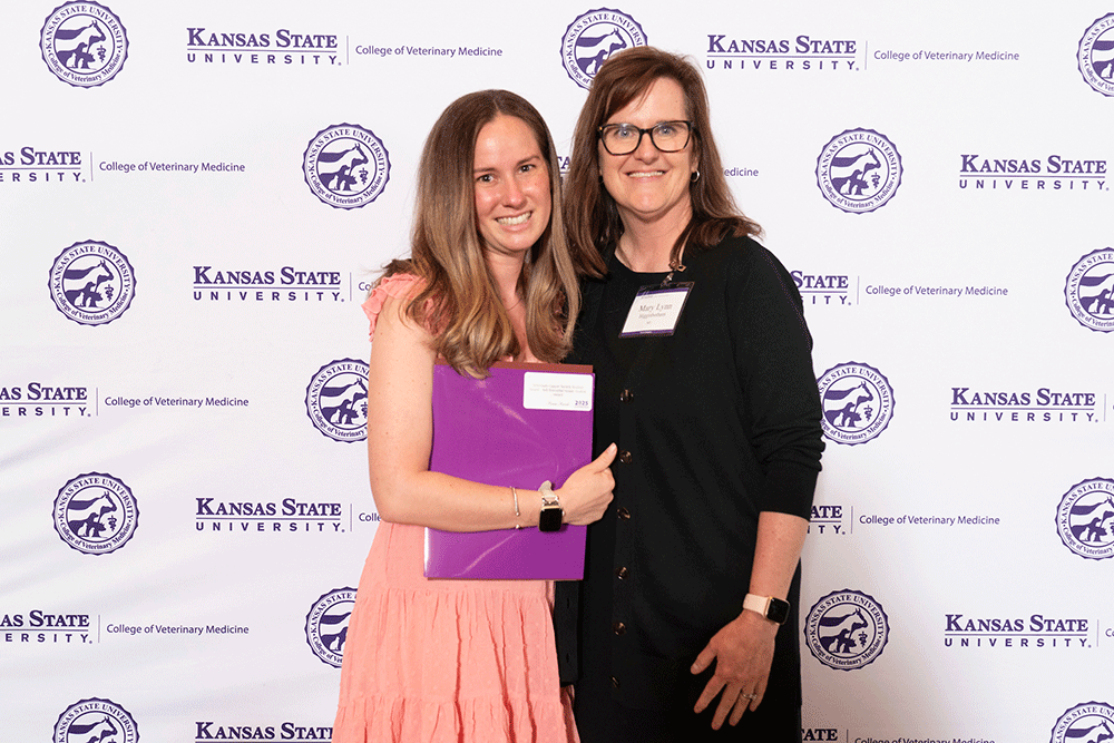 Two people stand in front of a backdrop smiling.