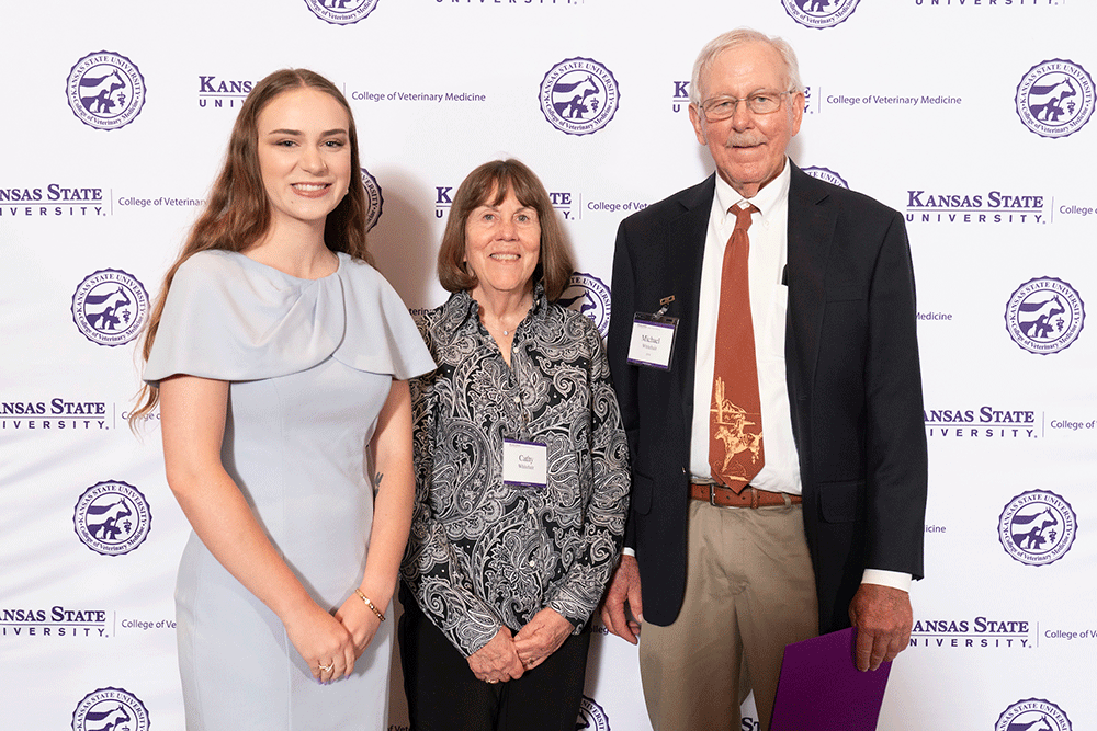 Three people stand in front of a backdrop smiling.