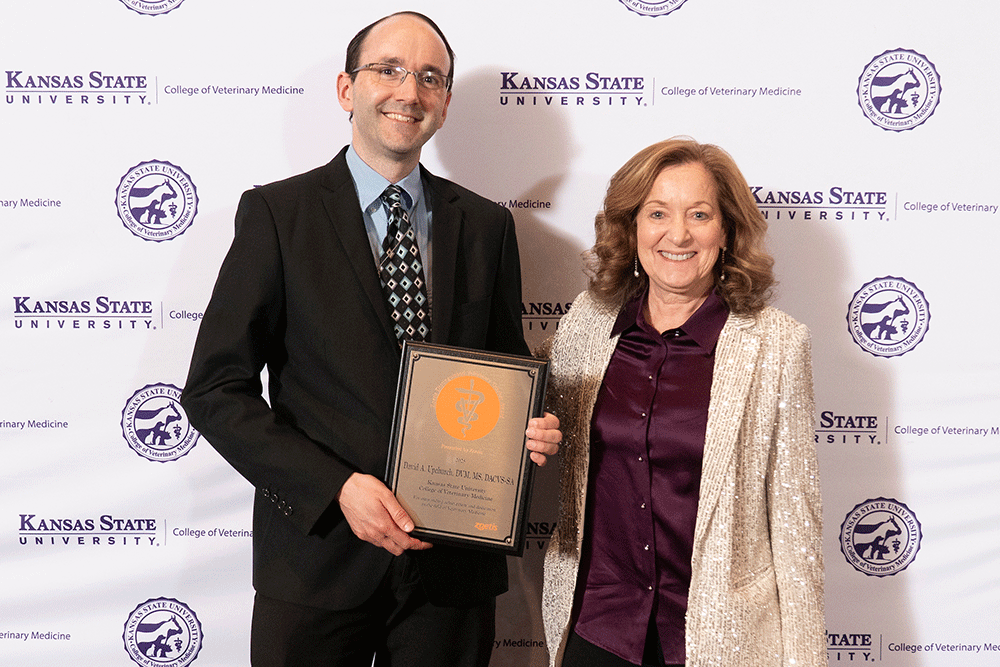 Two people stand in front of a backdrop smiling.