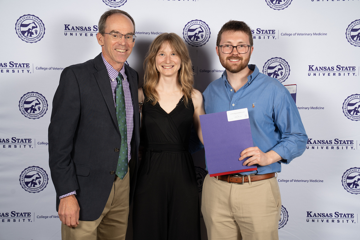 Three people stand in front of a backdrop smiling.