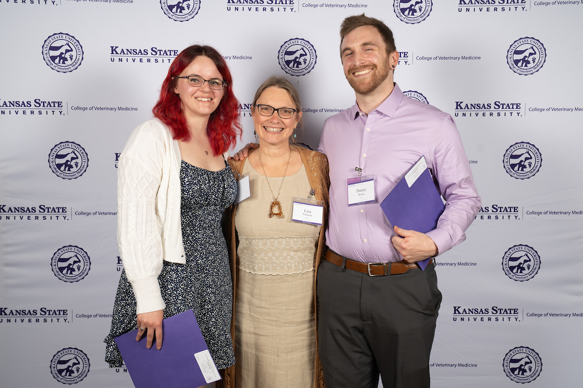 Three people stand in front of a backdrop smiling.