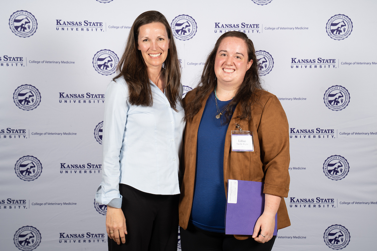 Two people stand in front of a backdrop smiling.