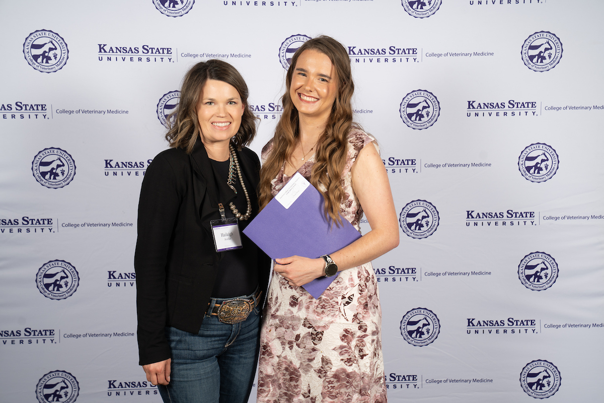 Two people stand in front of a backdrop smiling.